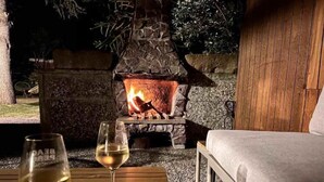 A cozy outdoor seating area with a stone fireplace, a wooden table, and a glass of white wine. - Quiet, comfortable apartment near the beach (Sankt Peter-Ording)