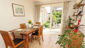 A dining area with a wooden table set for four, chairs, a vase with flowers, and a view through a glass door to an outdoor patio. - 14 Shorwell (Southampton)