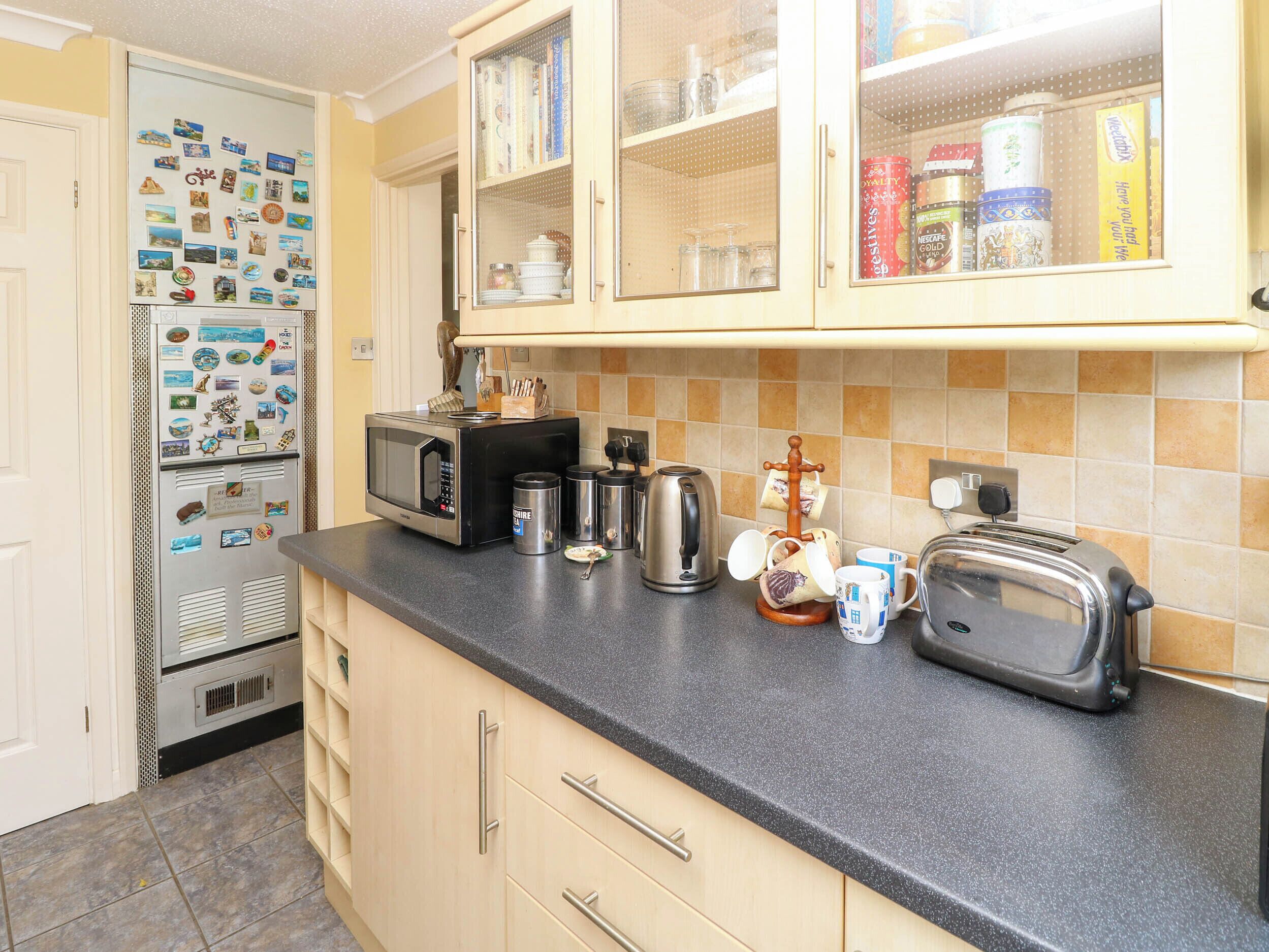 A kitchen with a refrigerator, microwave, toaster, and various kitchen items on the counter.