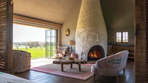 A cozy living room with a fireplace, a large window, and a view of the outdoors. - Wilderness Reserve - Hayjack (Saxmundham)