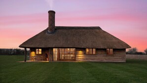 A thatched-roof house with a chimney, large windows, and a grassy lawn. - Wilderness Reserve - Hayjack (Saxmundham)