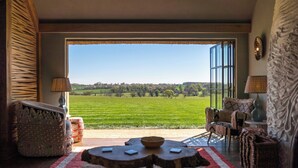 A living room with a large window, a round wooden table, and a view of a green field. - Wilderness Reserve - Hayjack (Saxmundham)