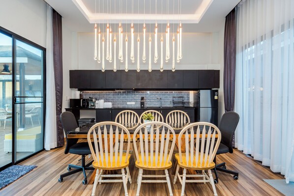 Un espace repas moderne avec une table et des chaises en bois, une cuisine en arrière-plan et de grandes fenêtres avec des rideaux.