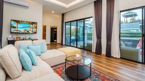 Ein modernes Wohnzimmer mit einem beigefarbenen Sofa, einem Glastisch und einem großen Fenster mit Vorhängen.