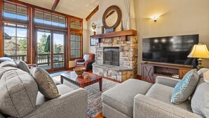A living room with a stone fireplace, a large flat-screen TV, and a cozy seating area with sofas and a coffee table. - Lady Luck by the Beach - Downtown Greystone unit with air conditioning (McCall)