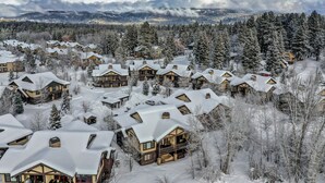 A snow-covered resort with multiple chalet-style buildings, surrounded by dense forests and mountains in the background. - Lady Luck by the Beach - Downtown Greystone unit with air conditioning (McCall)
