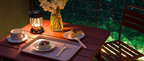 A dining table with a candle, a vase of flowers, a cake, and a cup.