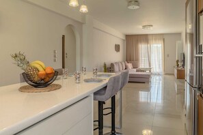 Uma cozinha moderna com uma ilha central, uma sala de jantar com um sofá e uma sala de estar com uma janela grande.