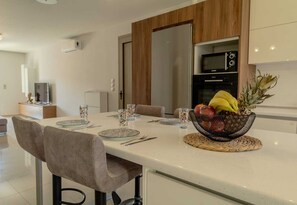 Una cocina moderna con comedor, que incluye un frutero en la encimera, un televisor al fondo y un horno microondas.