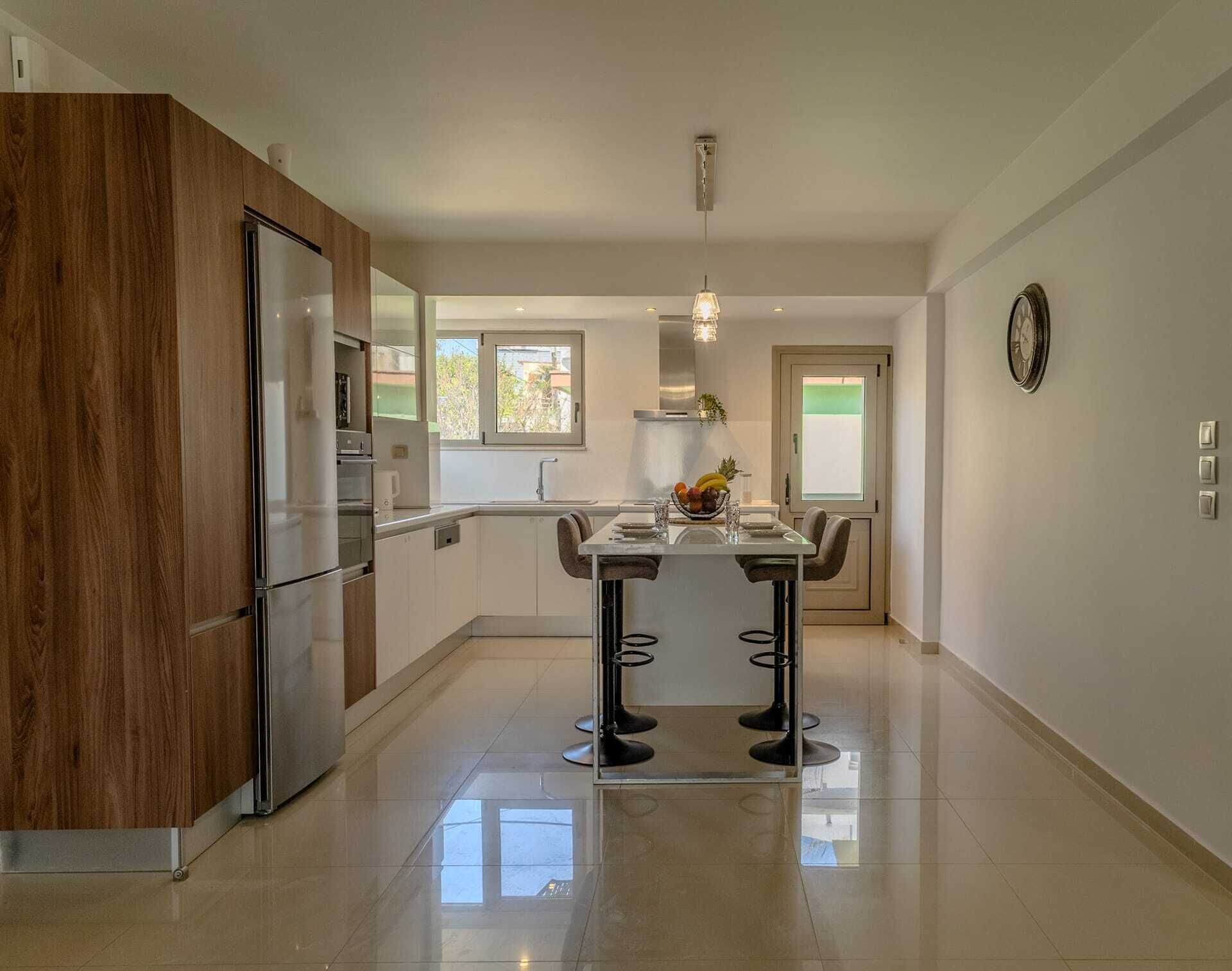 A modern kitchen with a central island, a wooden cabinet, and a dining area with chairs.