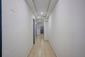 En lång, smal hall med vita väggar och ett kaklat golv, som leder fram till en rad dörrar i slutet.