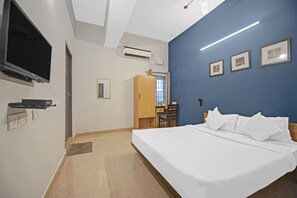 Ett hotellrum med en säng, ett skrivbord, en stol, en tv och inramade tavlor på väggen.