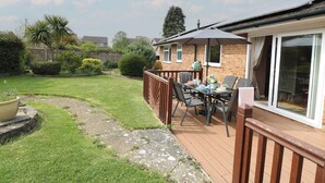 A patio area with a table and chairs, a wooden deck, and a brick house with a sliding glass door. - White Lion Retreat (Cromer)