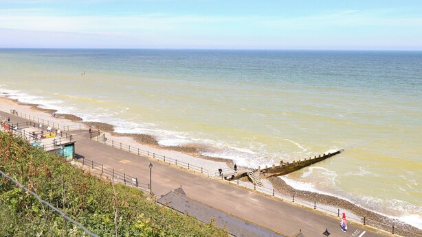A coastal road with a sea wall, a pedestrian walkway, and a rocky beach. - White Lion Retreat (Cromer)