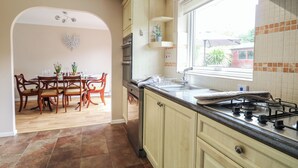 A kitchen with wooden cabinets, a gas stove, and a dining area with a table and chairs. - White Lion Retreat (Cromer)