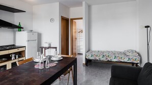 Une cuisine compacte équipée d’une cuisinière, d’un réfrigérateur et d’une table à manger agrémentée de verres. On aperçoit un lit recouvert d’une couvre-lit à motifs floraux au fond.