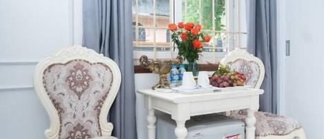 A room with two ornate chairs, a small table with a vase of flowers, and a window with curtains.