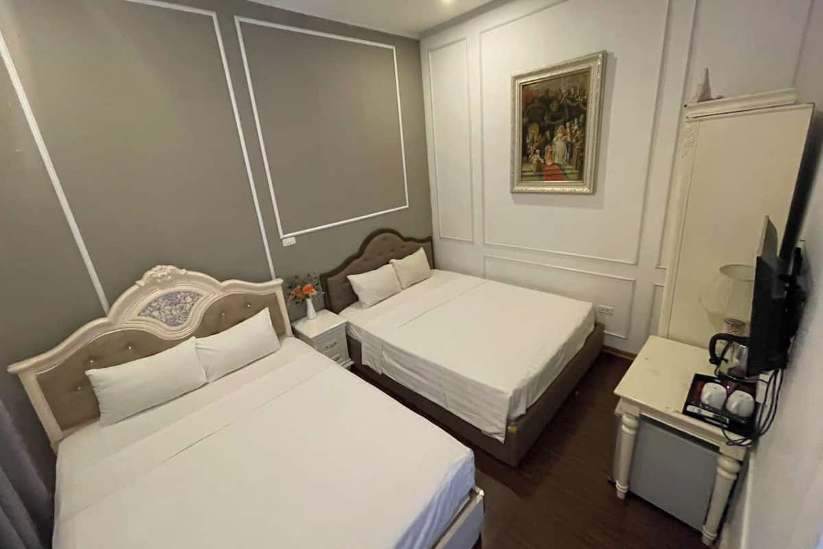 Una habitación de hotel con dos camas individuales, una mesita de noche con lámpara, un televisor y un cuadro en la pared.