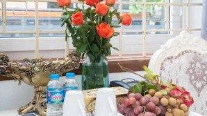 Een tafel met een vaas rode rozen, een fles water, een bord met eten, en een dienblad met druiven en ander fruit.