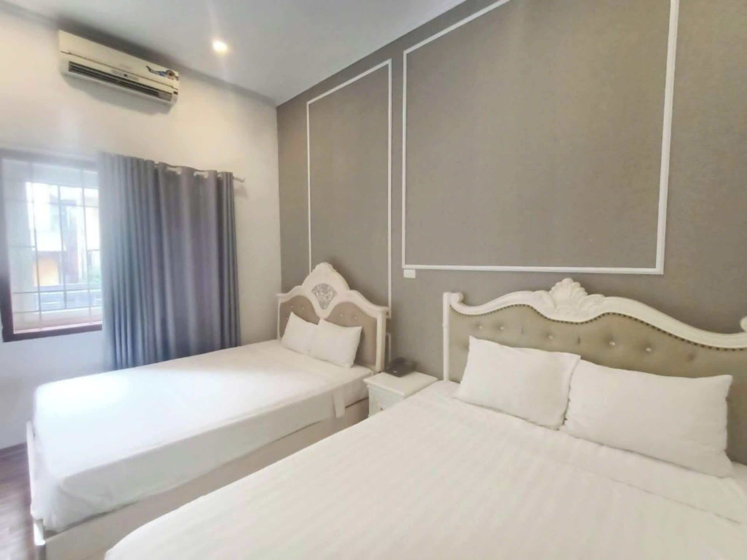 Une chambre d’hôtel avec deux lits, une fenêtre avec des rideaux, un appareil de climatisation et un cadre photo fixé au mur.