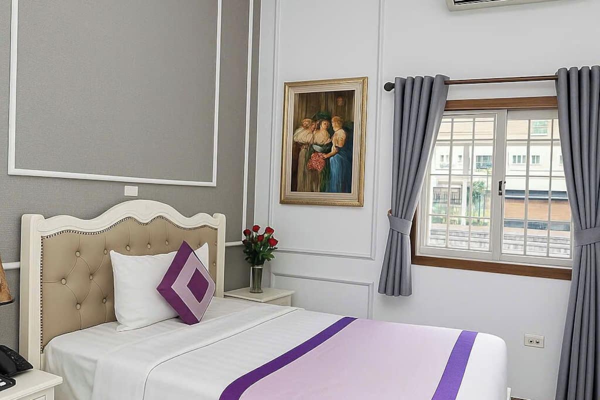 Un dormitorio ordenado con cama, mesita de noche y ventana con cortinas.