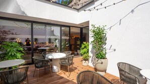 Un'area patio all'aperto con tavoli e sedie rotonde, piante in vaso e luci decorative.