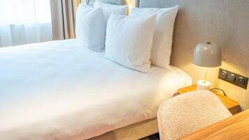 A neatly made bed with white linens and pillows, a bedside lamp, and a wooden nightstand.
