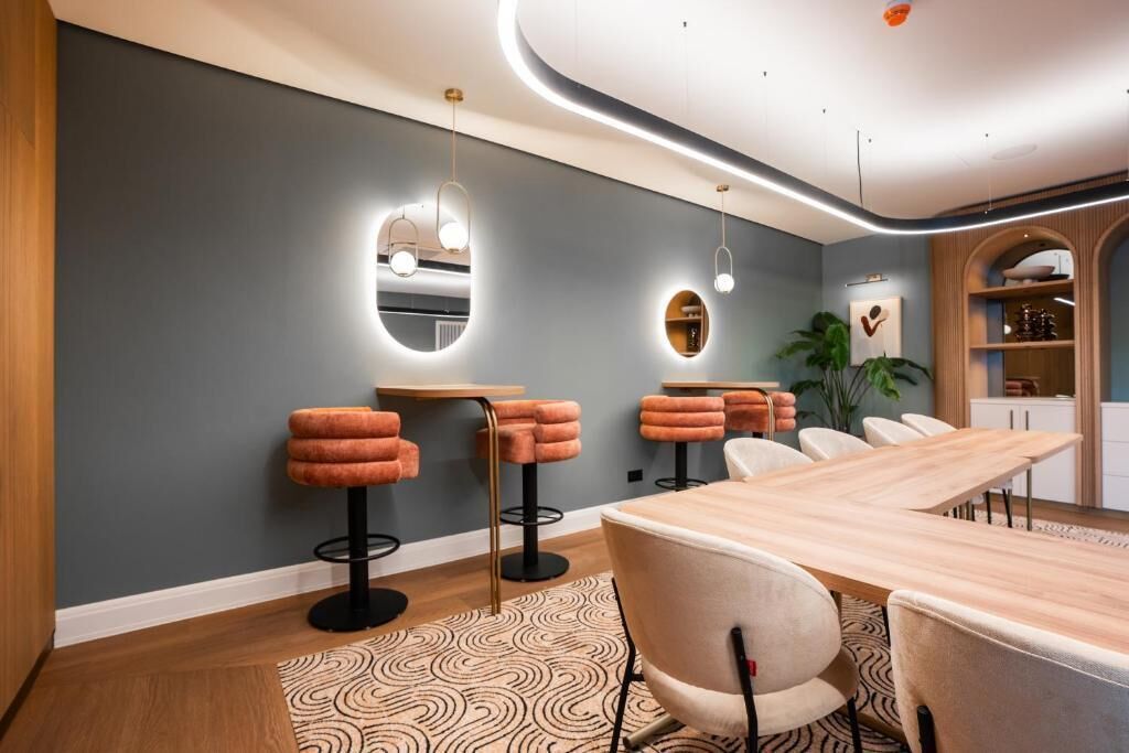 A modern dining area with a long wooden table, cushioned bar stools, and pendant lighting.