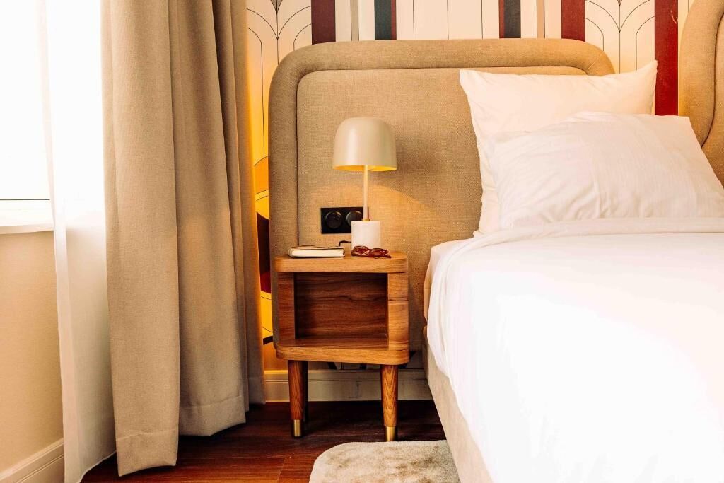 Una cama bien hecha con sábanas blancas, una mesita de noche de madera con una lámpara.