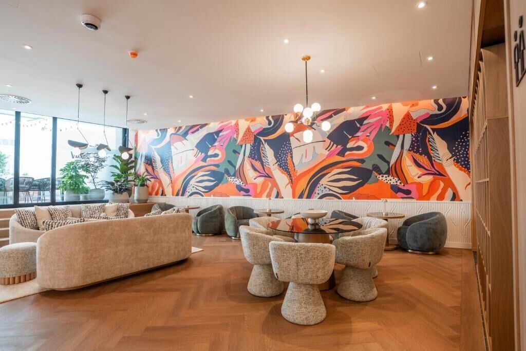 Un área de estar moderna con un mural abstracto lleno de color, asientos cómodos y vistas al exterior.