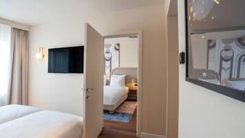 Habitació d'hotel amb un llit, televisió penjada a la paret i una porta que dona a una altra habitació.