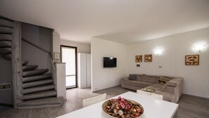 A modern living room with a staircase, a flat-screen TV, and a dining area with a table and chairs. - Villa Golf in Polpenazze del Garda (Polpenazze del Garda)