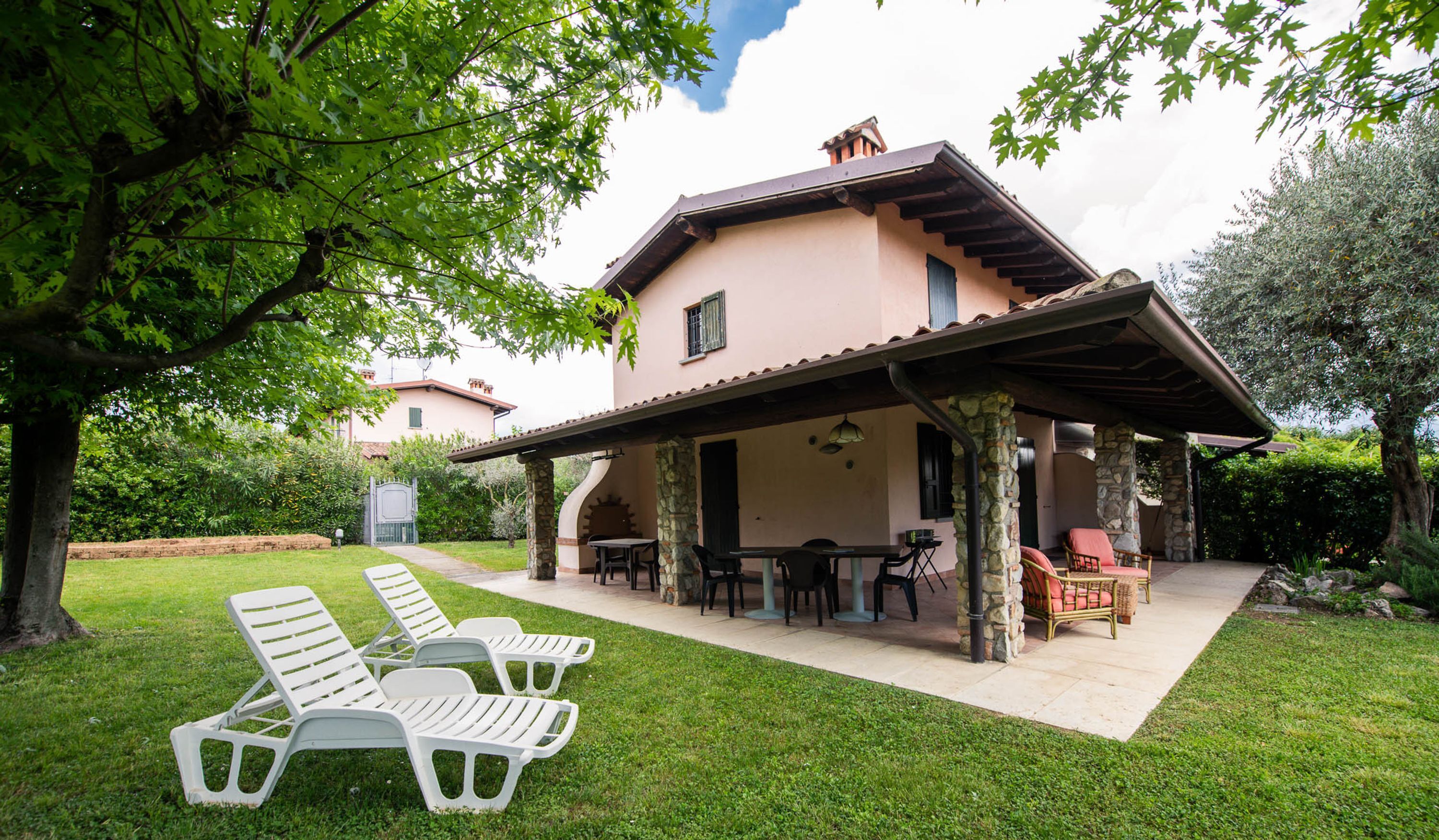 A two-story house with a covered patio area, outdoor seating, and a lawn with lounge chairs.