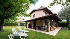 A two-story house with a covered patio area, outdoor seating, and a lawn with lounge chairs. - Villa Golf in Polpenazze del Garda (Polpenazze del Garda)
