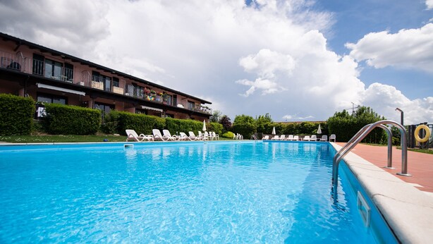 A swimming pool with lounge chairs and a building with balconies in the background. - Villa Golf in Polpenazze del Garda (Polpenazze del Garda)