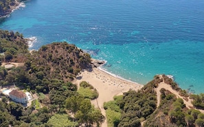 Vue aérienne d’une zone côtière avec une plage, un petit bâtiment et une végétation dense.
