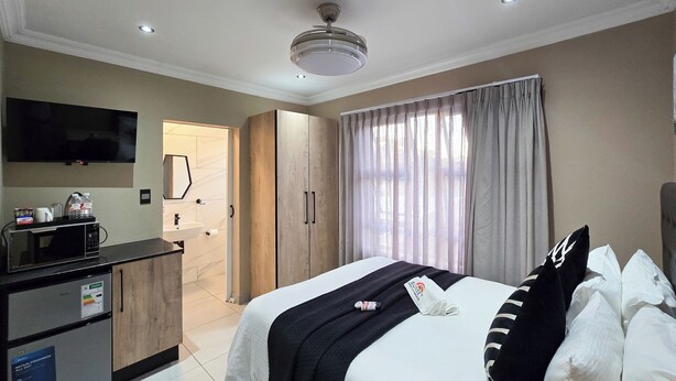 Habitación de hotel con cama, televisión, minibar, baño y una ventana grande con cortinas.