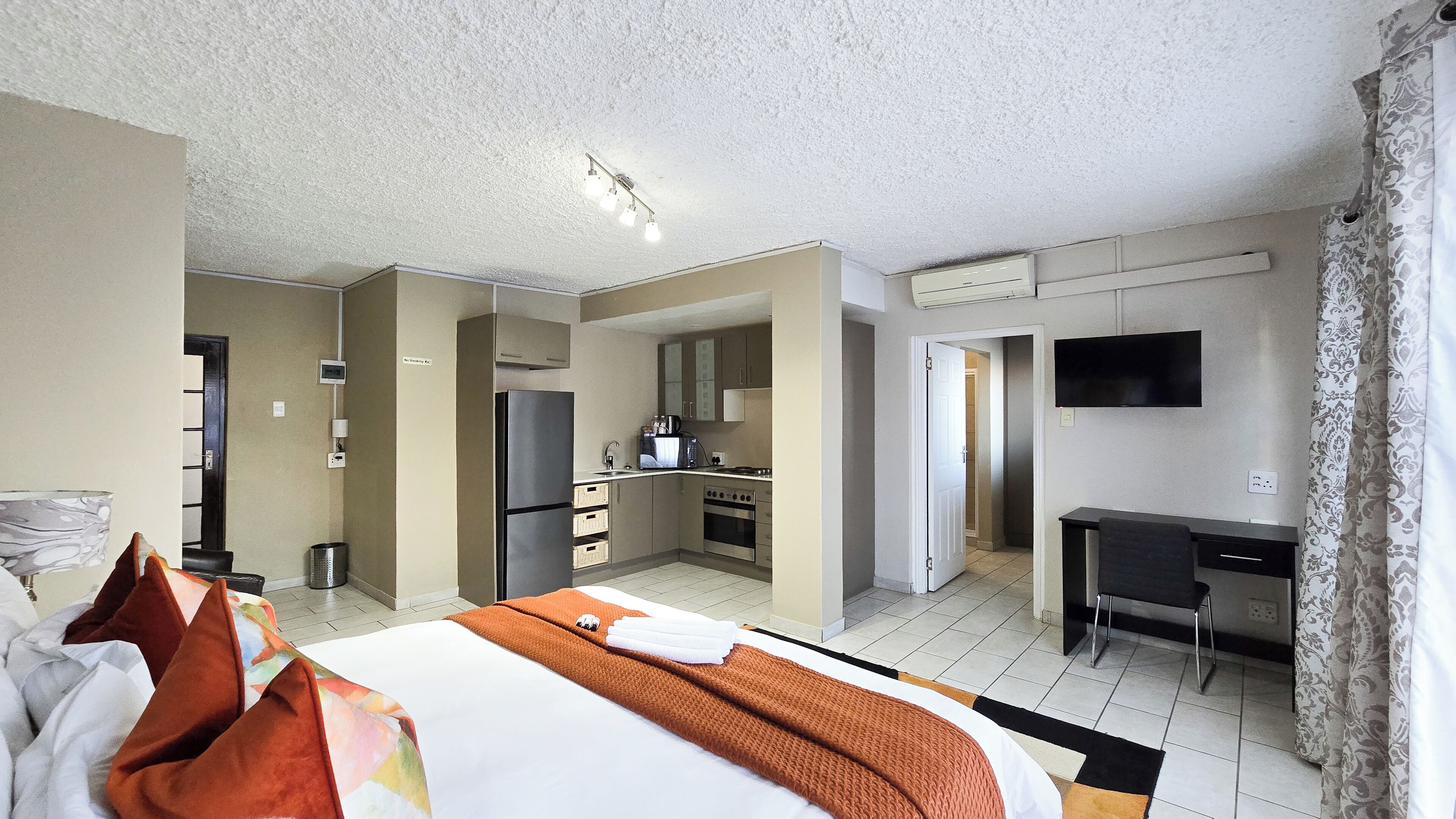 A hotel room with a bed, a desk, a kitchenette, and a TV.