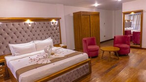 Ein Hotelzimmer mit einem großen Bett, einem Holzschrank, zwei rosa Sesseln, einem kleinen runden Tisch und einem Spiegel.
