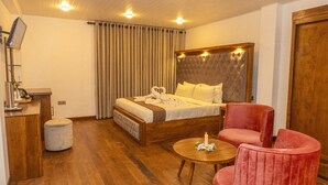 Ein Hotelzimmer mit einem großen Bett, einem Holzkopfende, einem Schreibtisch mit Lampe, einem runden Tisch mit Kerze und einem roten Stuhl.