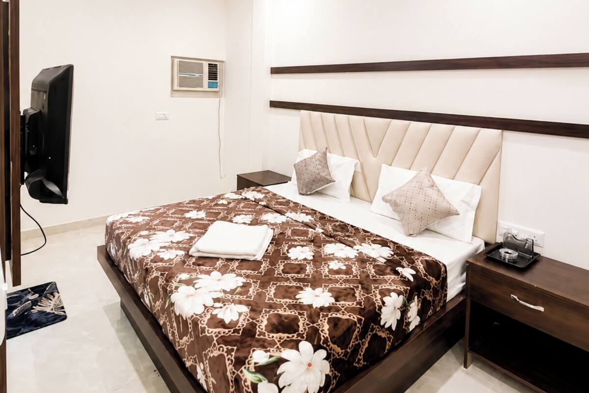 A hotel room with a bed, a ceiling fan, a TV, a bedside table, and a nightstand.
