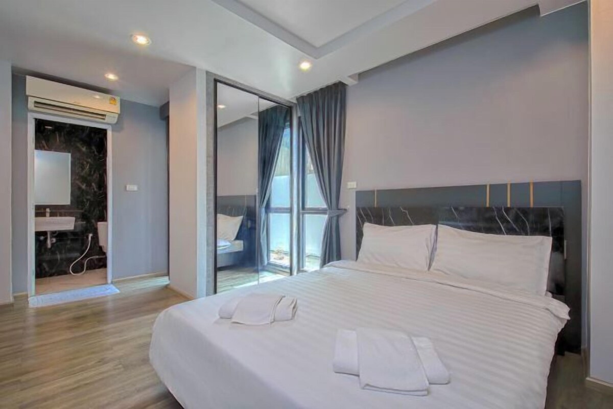 A modern hotel room with a large bed, a bathroom with a marble vanity, and a sliding glass door leading to a balcony.
