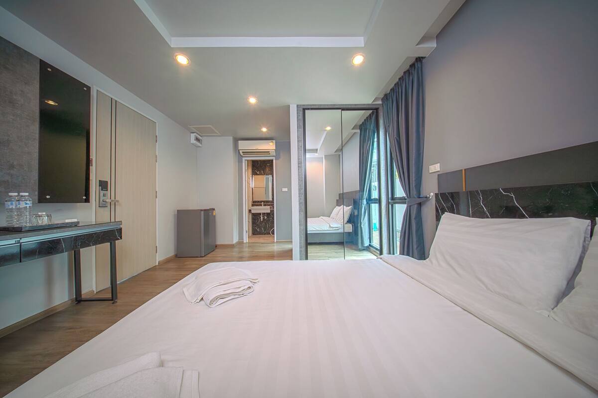 A modern hotel room with a large bed, a desk, and a bathroom visible through an open door.