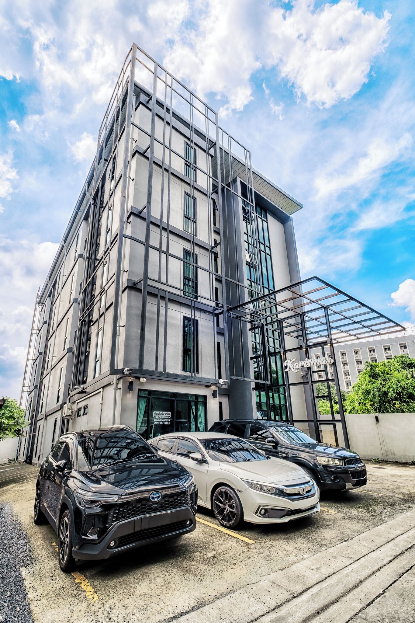 Un edificio moderno con fachada de vidrio y un estacionamiento con tres coches.