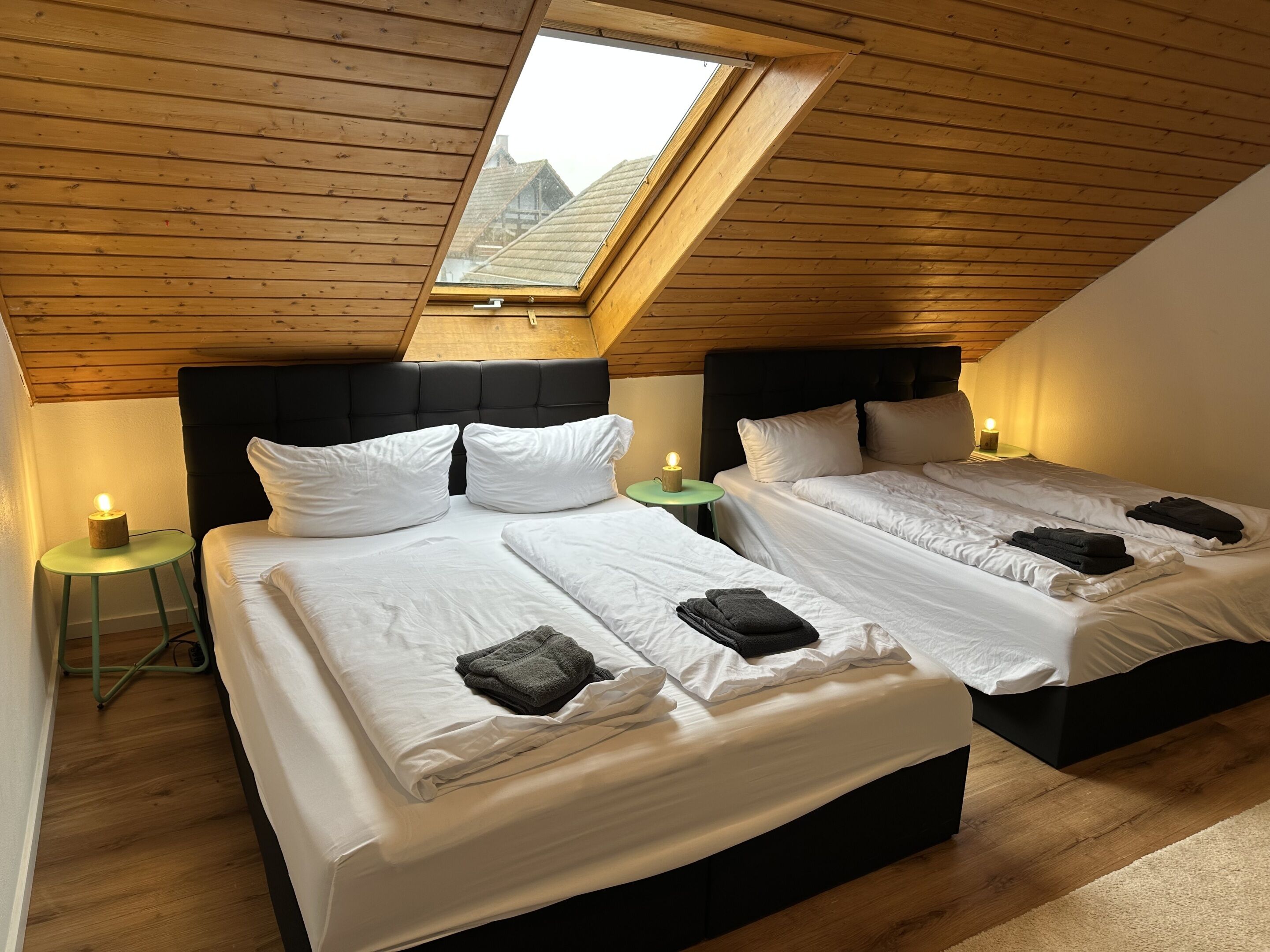 Una habitación con dos camas, techo de madera y tragaluz.