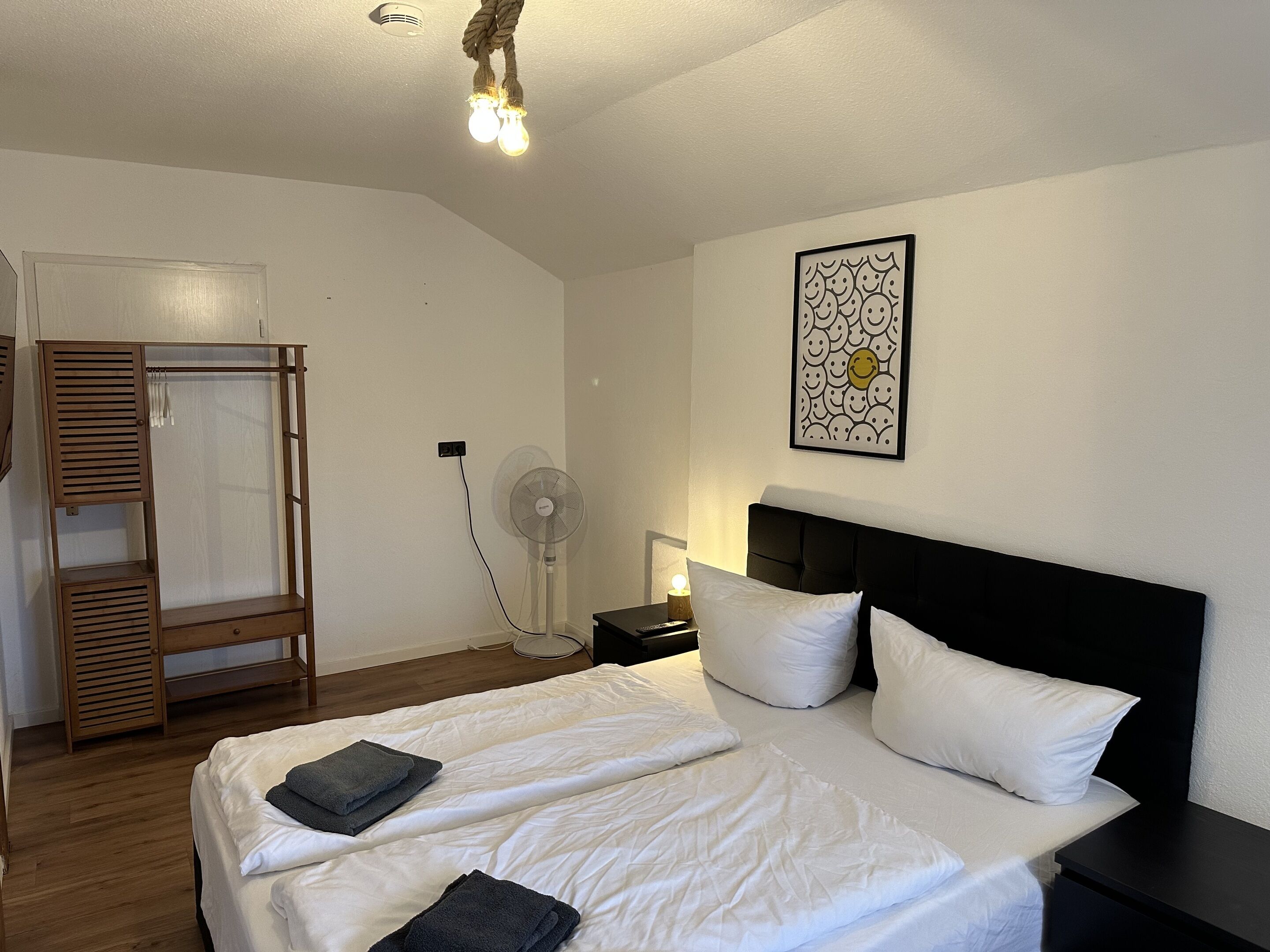 Un dormitorio con cama, mesita de noche, ventilador y armario.