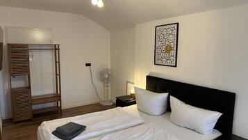 Un dormitorio con cama, mesita de noche, ventilador y armario.