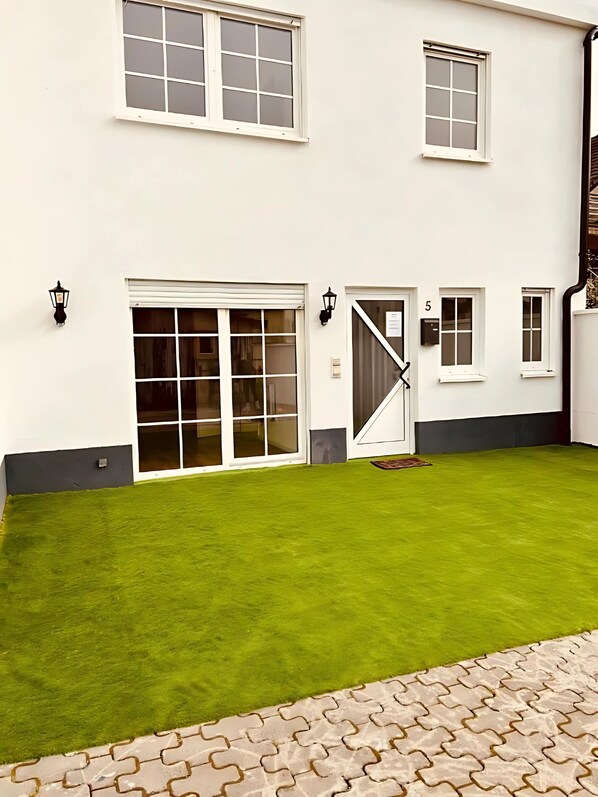 A white building with multiple windows, a green lawn, and a paved entrance.