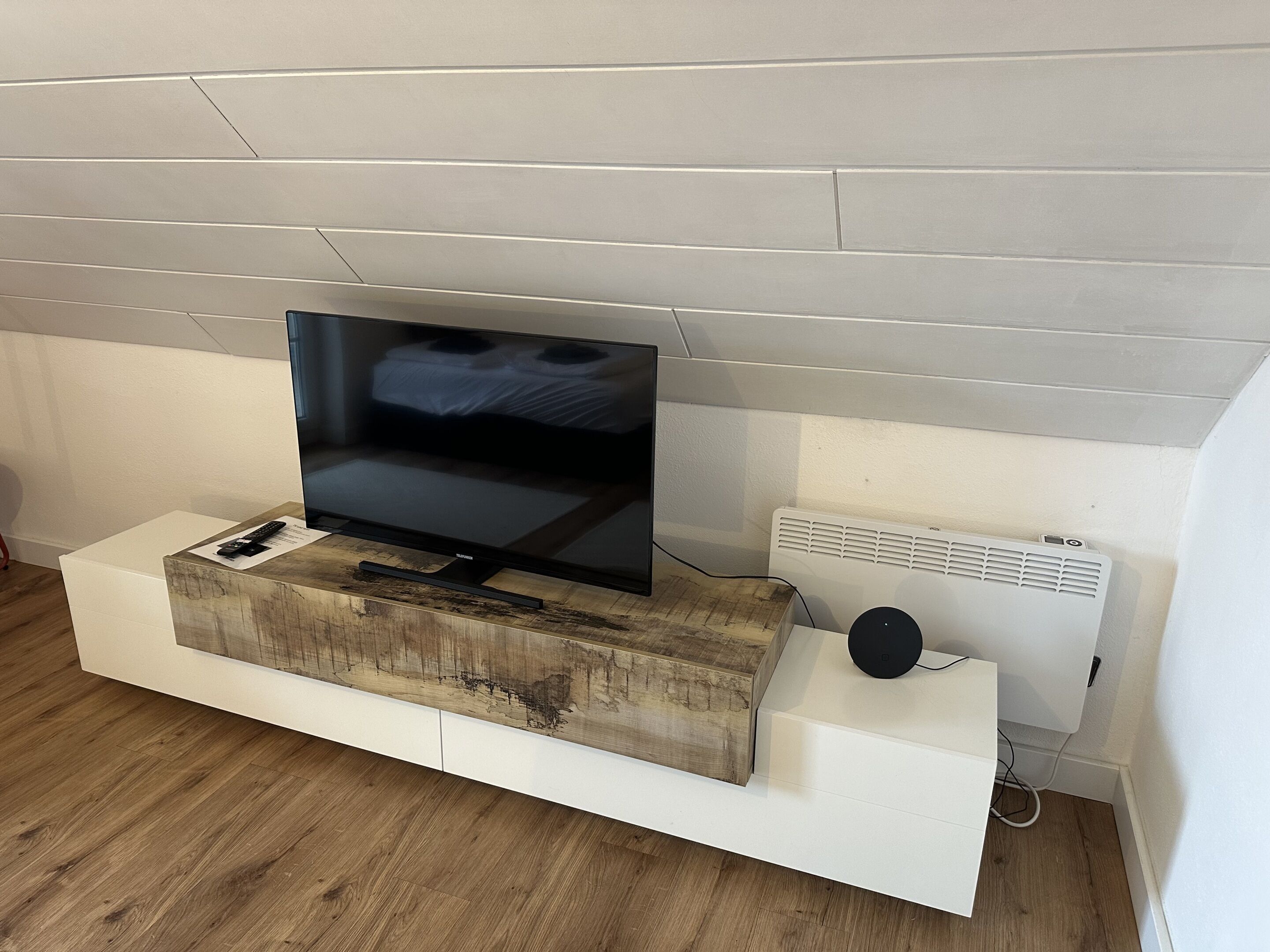 A flat-screen TV on a wooden TV stand against a white wall.
