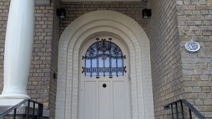 Une porte blanche avec un portail en métal noir, un mur de briques et une colonne blanche.